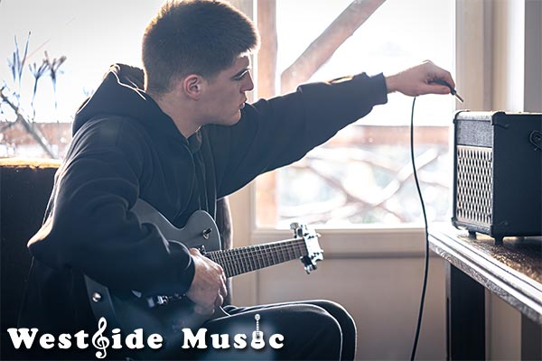 image of young man plugging in electric guitar.